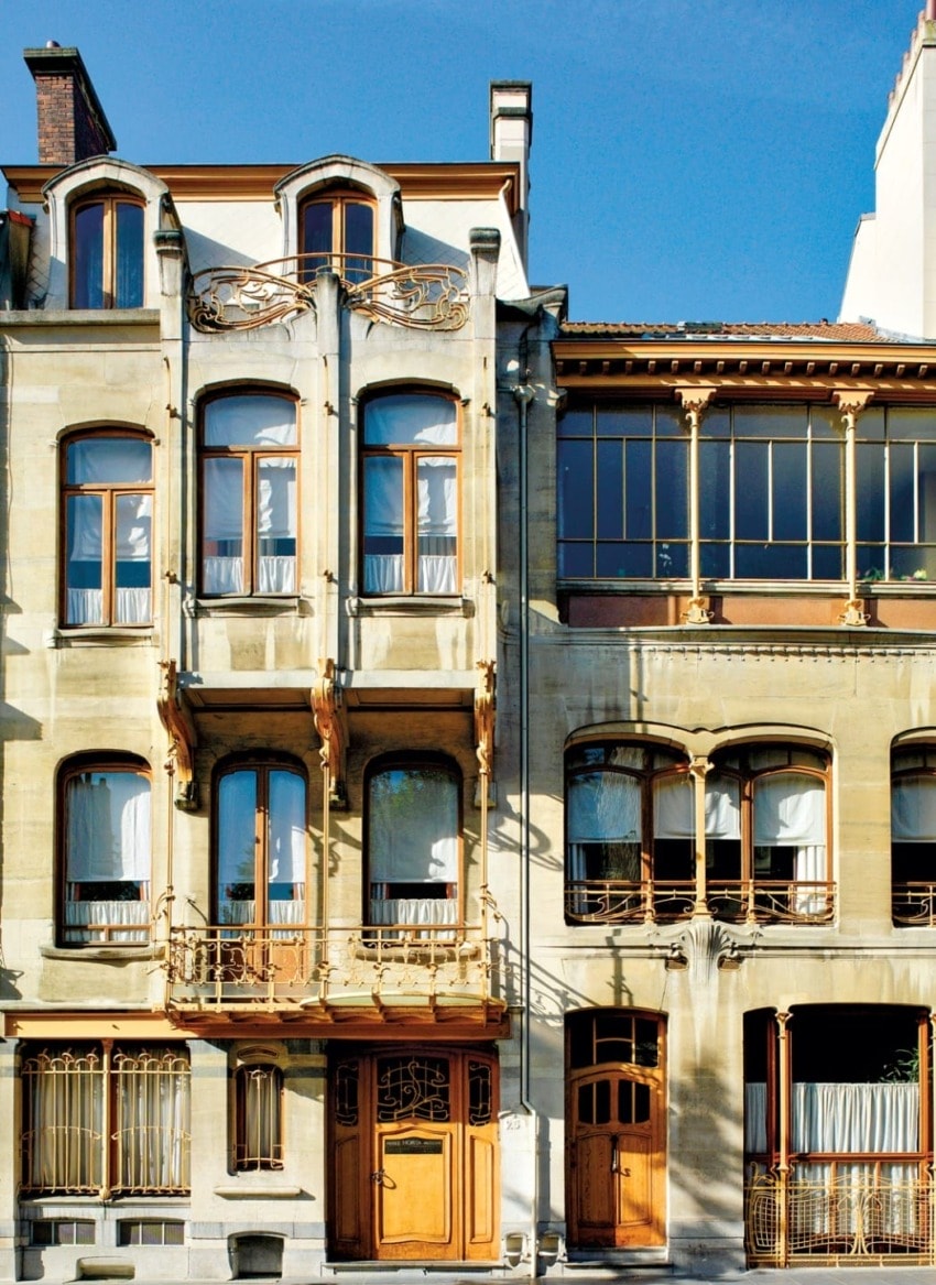 Facade of an Art Nouveau building with ornate ironwork and large wooden doors, under a clear blue sky.
