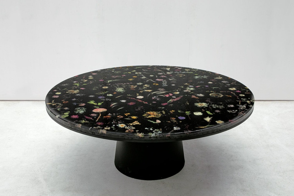 Round black table with intricate floral patterns on the surface, set against a plain white backdrop.