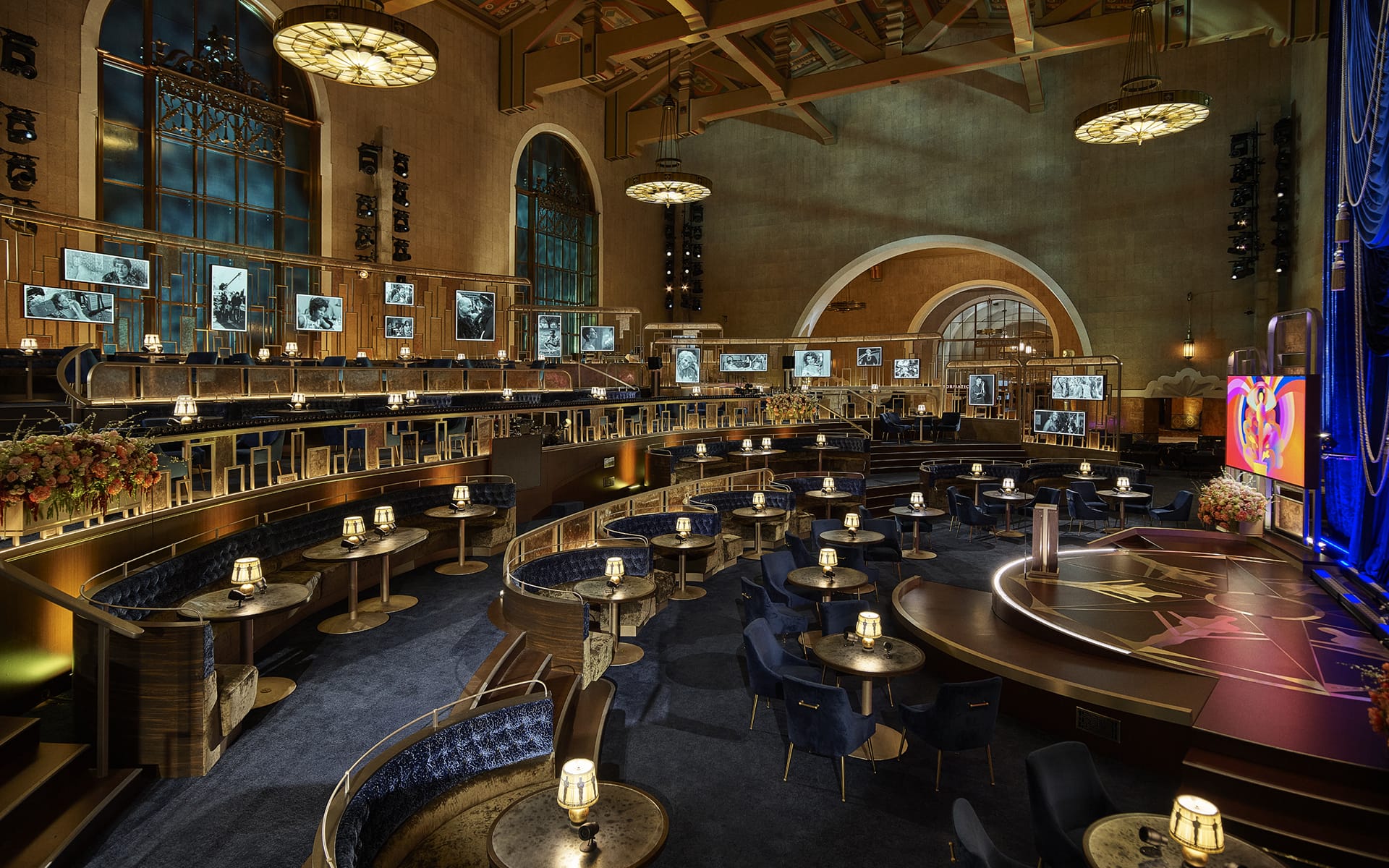 Luxurious banquet hall with round tables, elegant lighting, and large screens displaying black-and-white photos.
