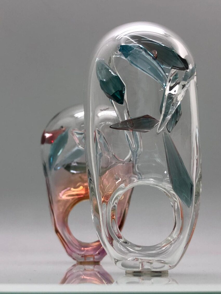 Two abstract glass sculptures with colorful embedded shapes on a reflective surface.