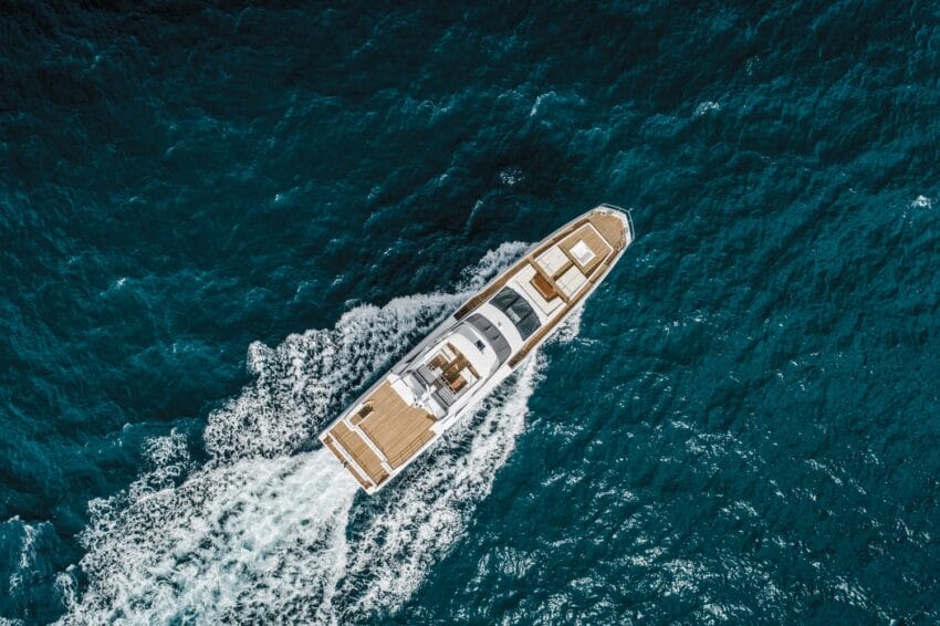 Aerial view of a luxurious yacht cruising through deep blue ocean waters, leaving a trail of white foam behind.