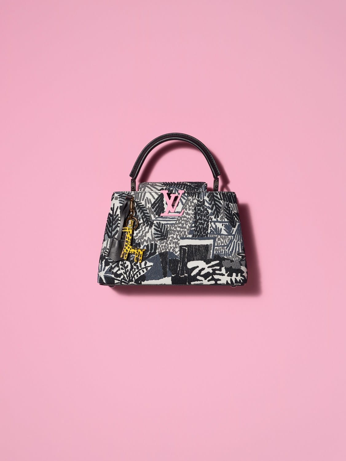 Luxury patterned handbag with dark handles and pink logo on soft pink background.