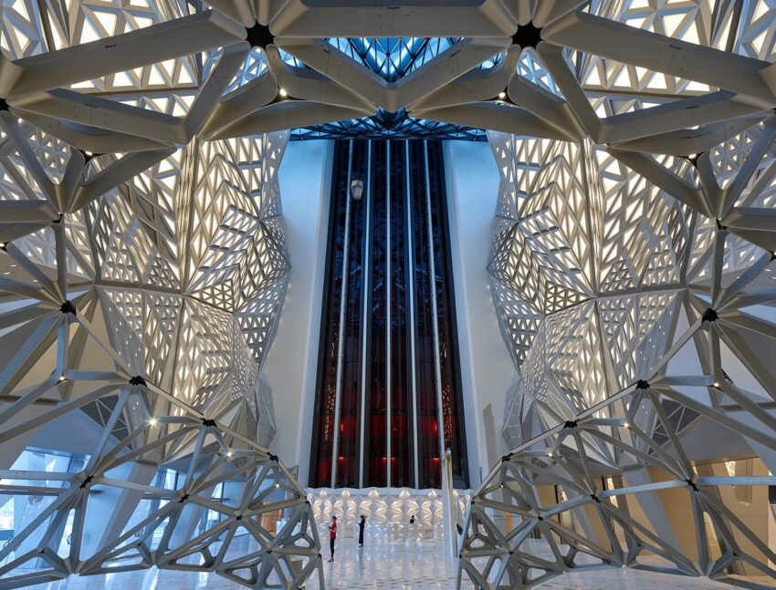 Futuristic building interior with geometric design and intricate lattice patterns, featuring a tall central atrium.