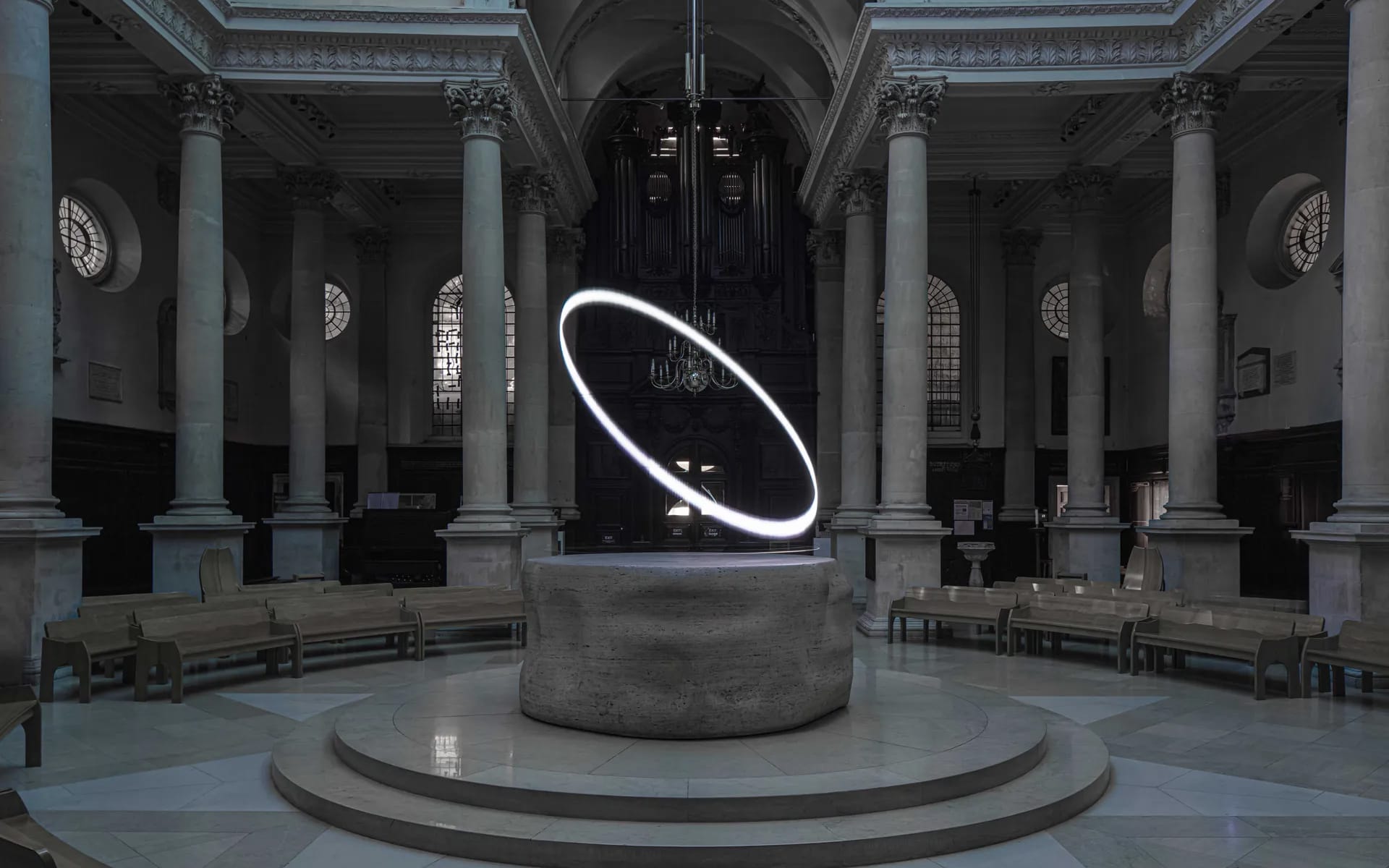 Illuminated ring sculpture hovering over stone altar in dark, ornate cathedral interior with tall columns and arched windows.