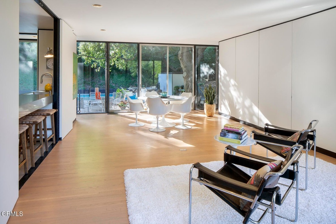 modern living and dining area with large windows, white chairs, and table; open layout with garden view