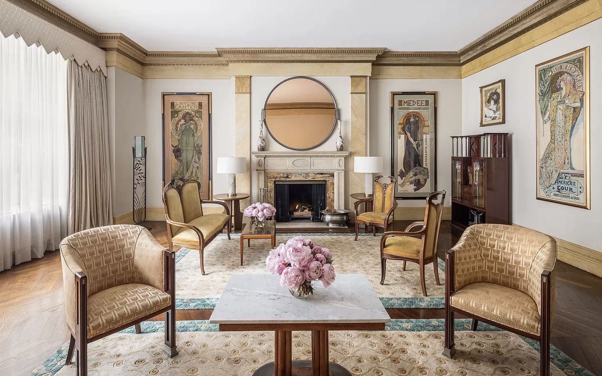 Elegant living room with vintage armchairs, a marble coffee table, floral centerpiece, and ornate fireplace with artwork.