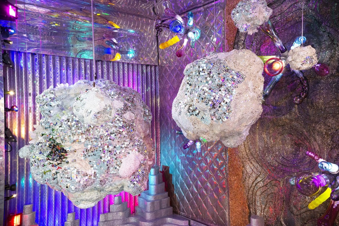 Colorful, abstract art installation featuring reflective clouds, neon lights, and textured surfaces in a vibrant setting.