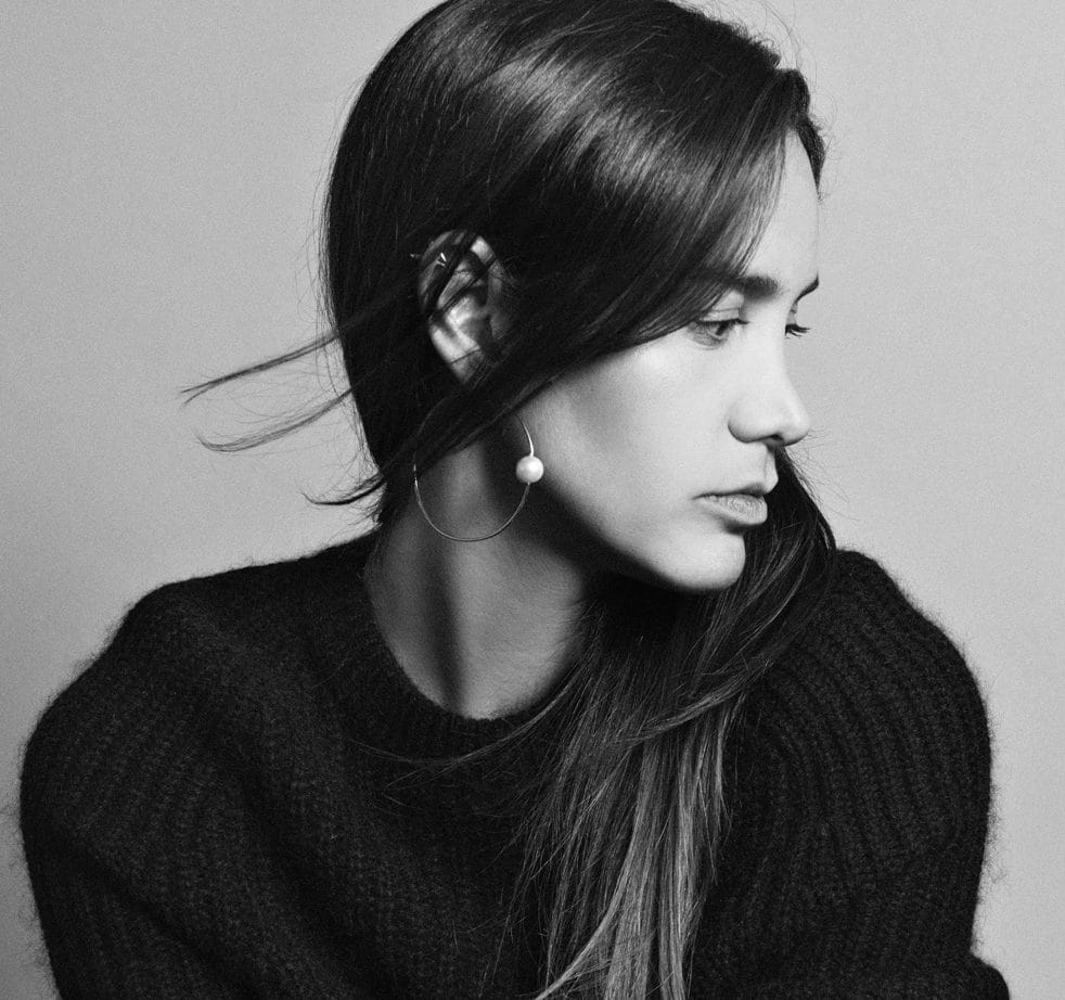 Woman in black sweater with long hair, looking sideways, wearing a round earring, monochrome portrait.