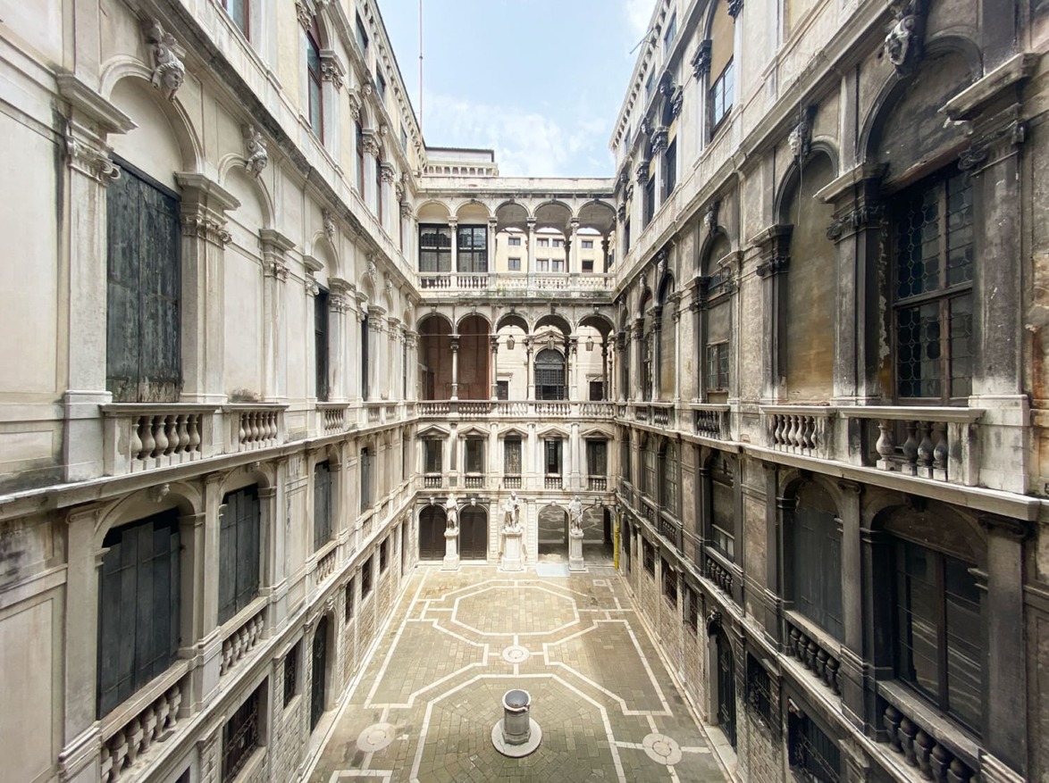 Interior of an old stone courtyard with arched windows and a central well, surrounded by multi-story buildings.