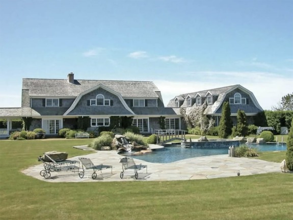 Large country home with a pool, patio, and manicured lawn on a sunny day.