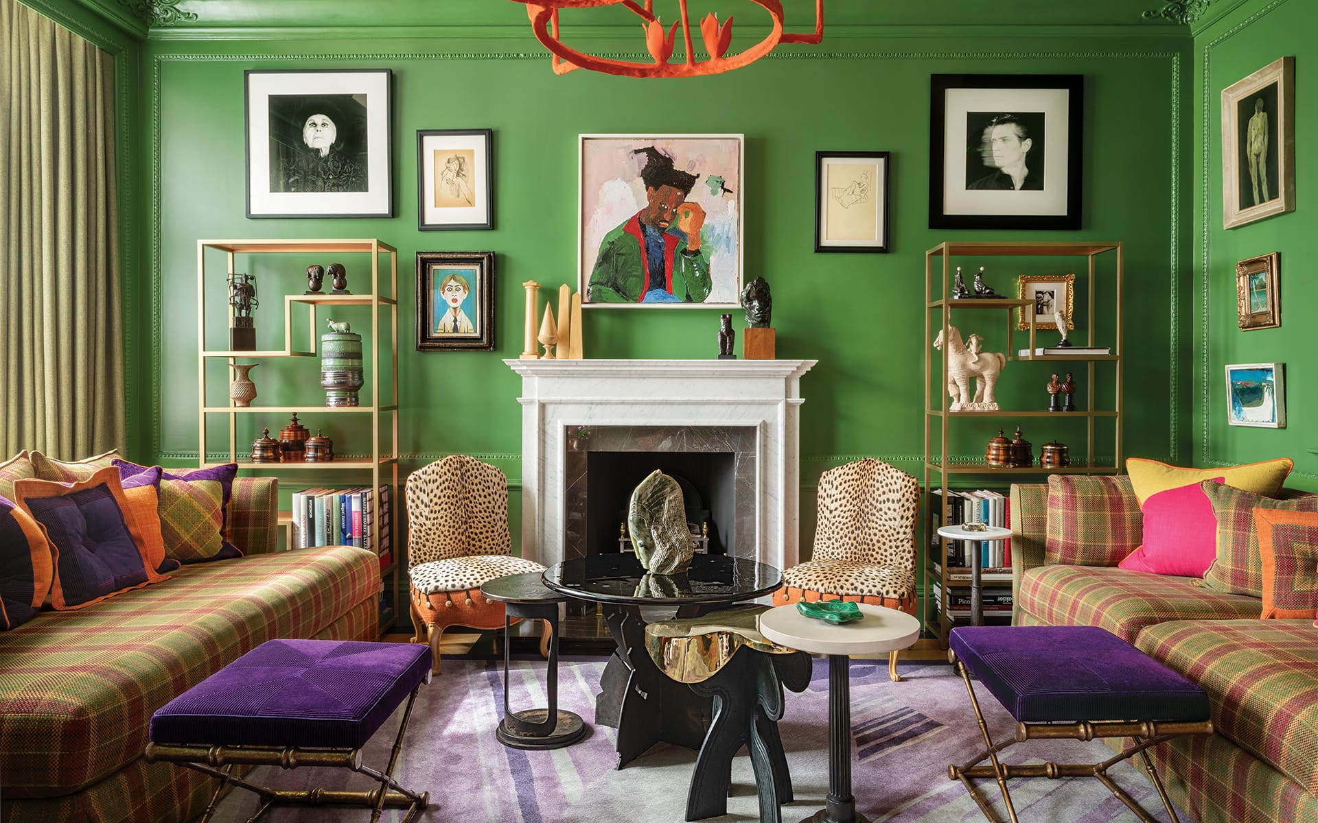 Eclectic living room with green walls, plaid sofas, vibrant art, and a fireplace surrounded by eclectic decor and sculptures.