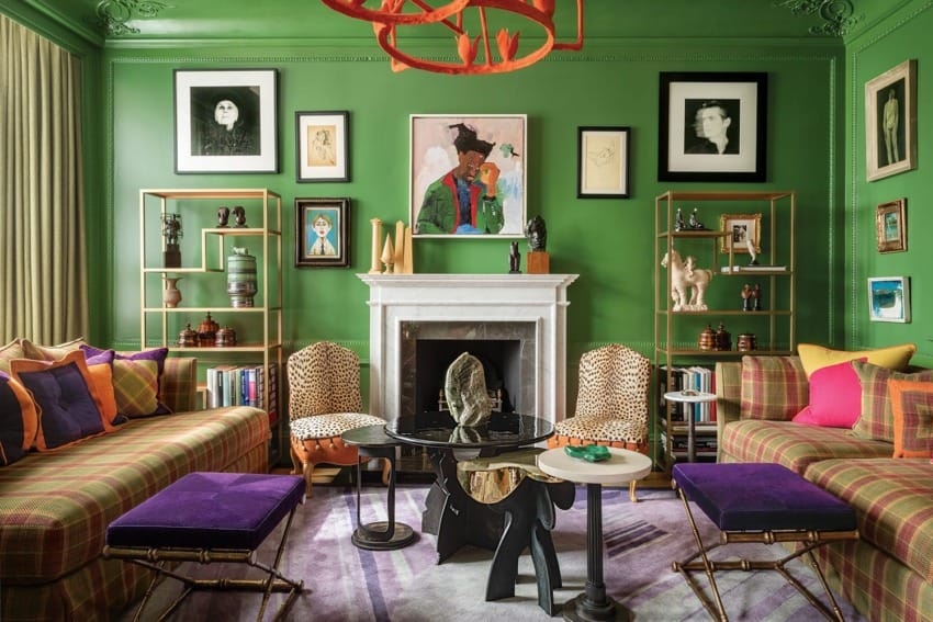 Colorful living room with green walls, eclectic artwork, patterned furniture, and vibrant decor around a central fireplace.