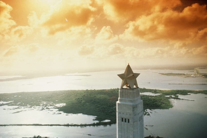 Tower with a large star top against a dramatic orange sky, overlooking a landscape of water and greenery.