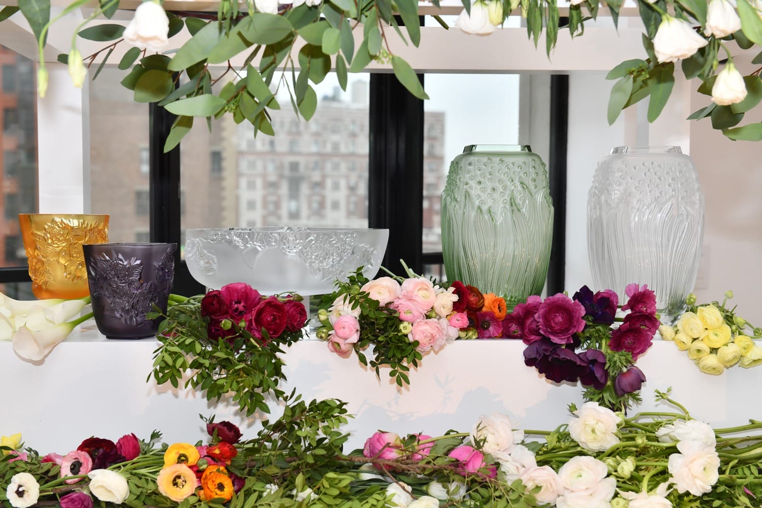 Colorful floral arrangements and decorative vases displayed on a windowsill with a cityscape backdrop.