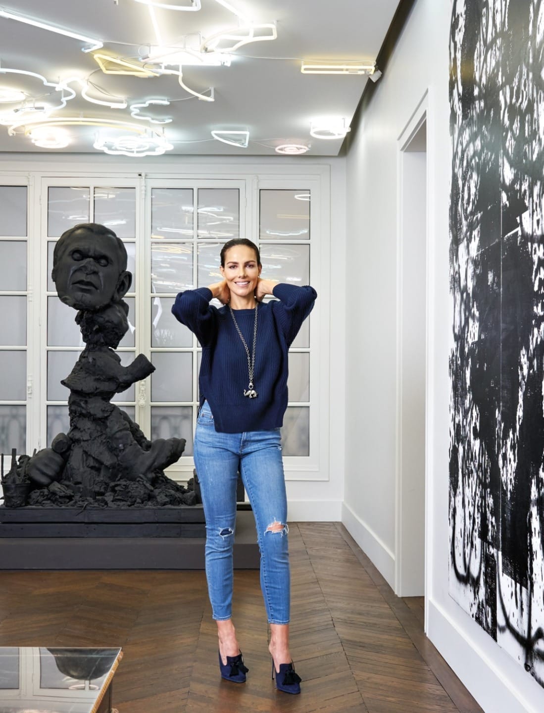 Person wearing a navy sweater and jeans standing in an art gallery with modern sculptures and abstract paintings.