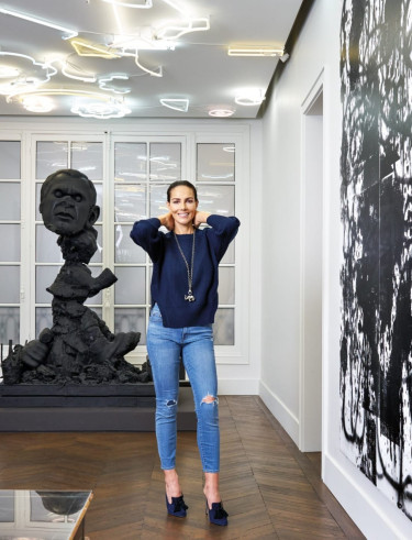 Person wearing a navy sweater and jeans standing in an art gallery with modern sculptures and abstract paintings.