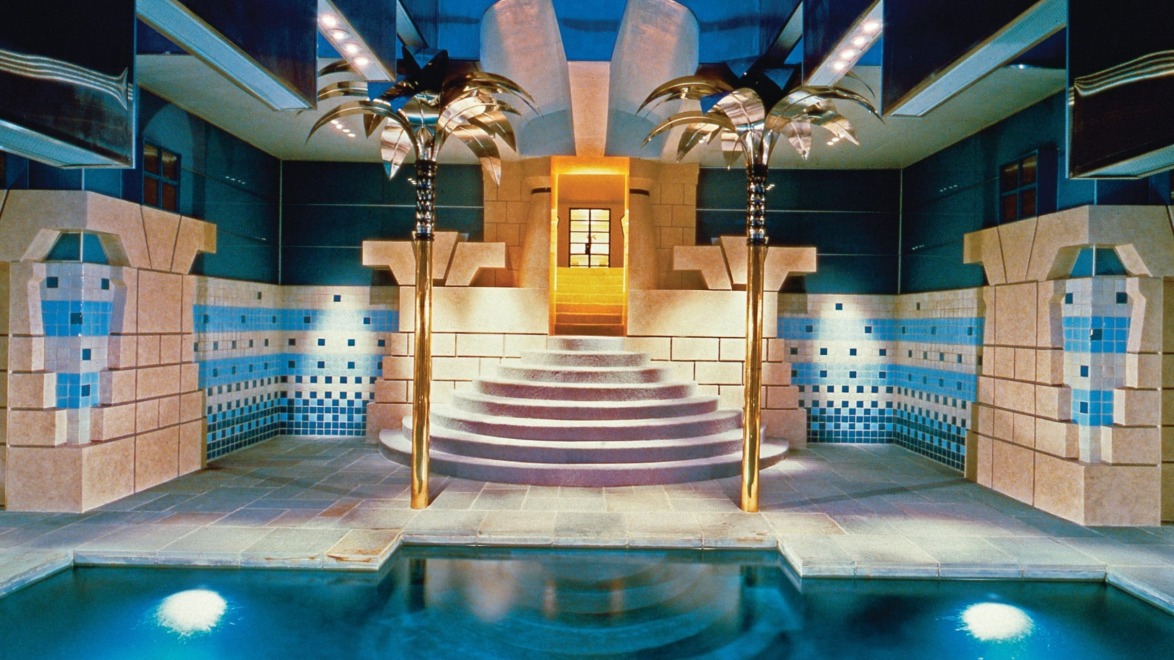 Luxurious indoor pool with ornate columns, decorative tiles, and ambient lighting in an elegant architectural setting.