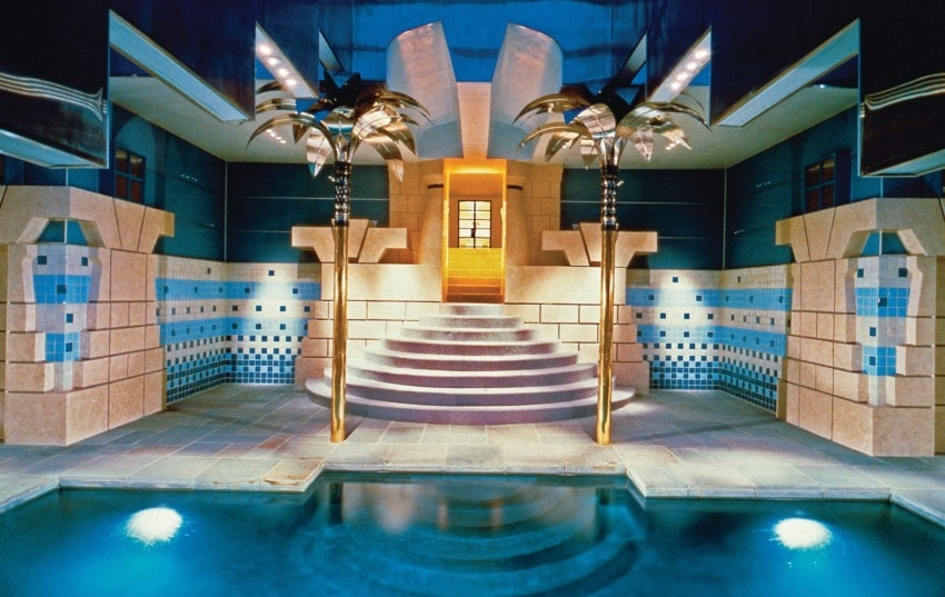 Luxurious indoor pool with ornate columns, decorative tiles, and ambient lighting in an elegant architectural setting.