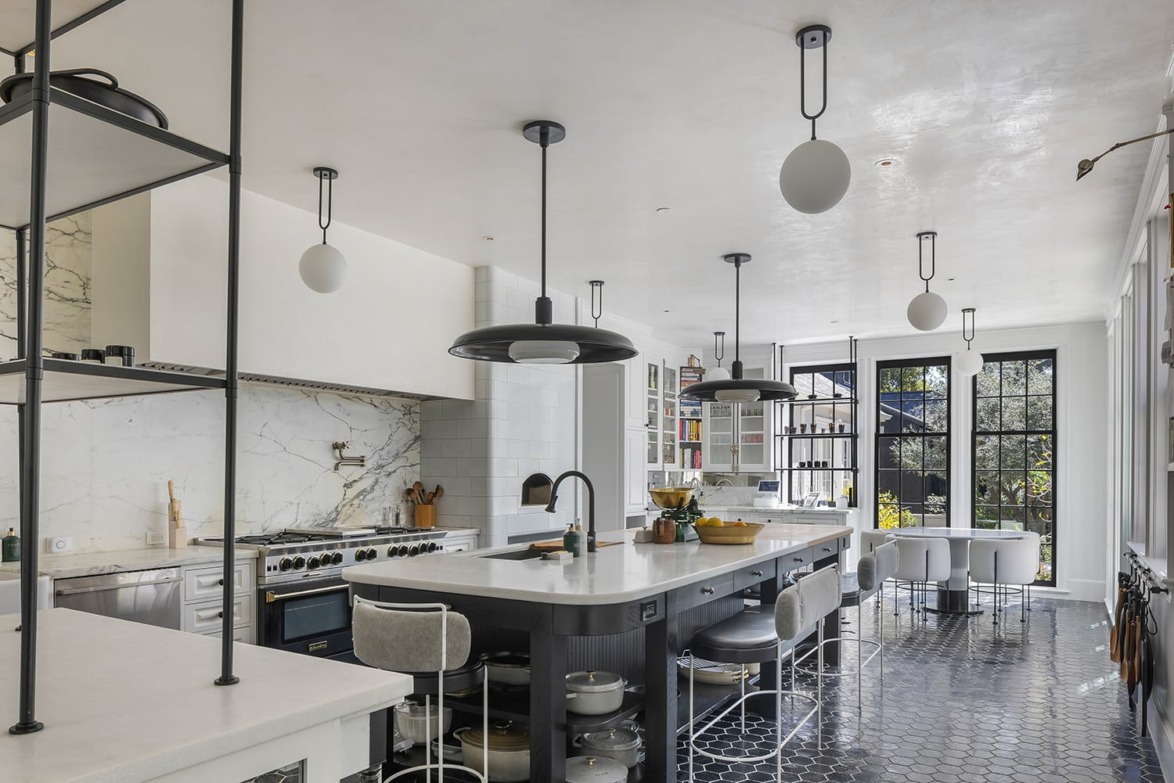 Modern kitchen with marble countertops, black pendant lights, hexagonal floor tiles, and large windows with garden view.