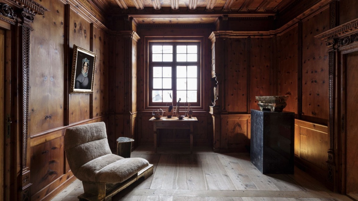 Wood-paneled room with a large window, an armchair, a pedestal display, and a painting on the wall.