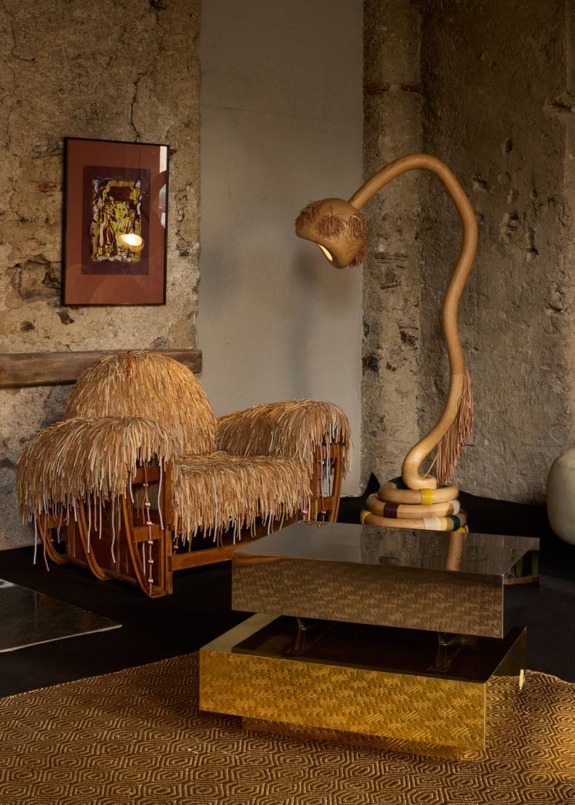 Eclectic room with a unique shaggy chair, organic-shaped floor lamp, and modern gold coffee table against a rustic wall.