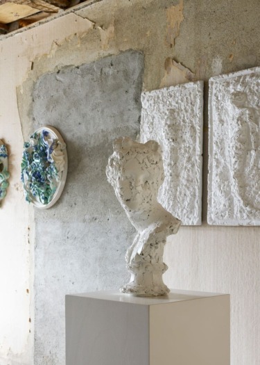 Abstract white sculptures on display against textured concrete and plaster walls in an art gallery setting