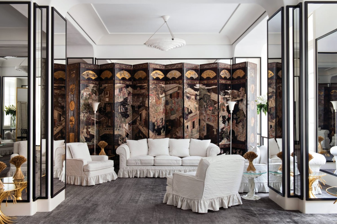 Elegant living room with white furniture, large decorative screen, mirrors, and gray carpet.