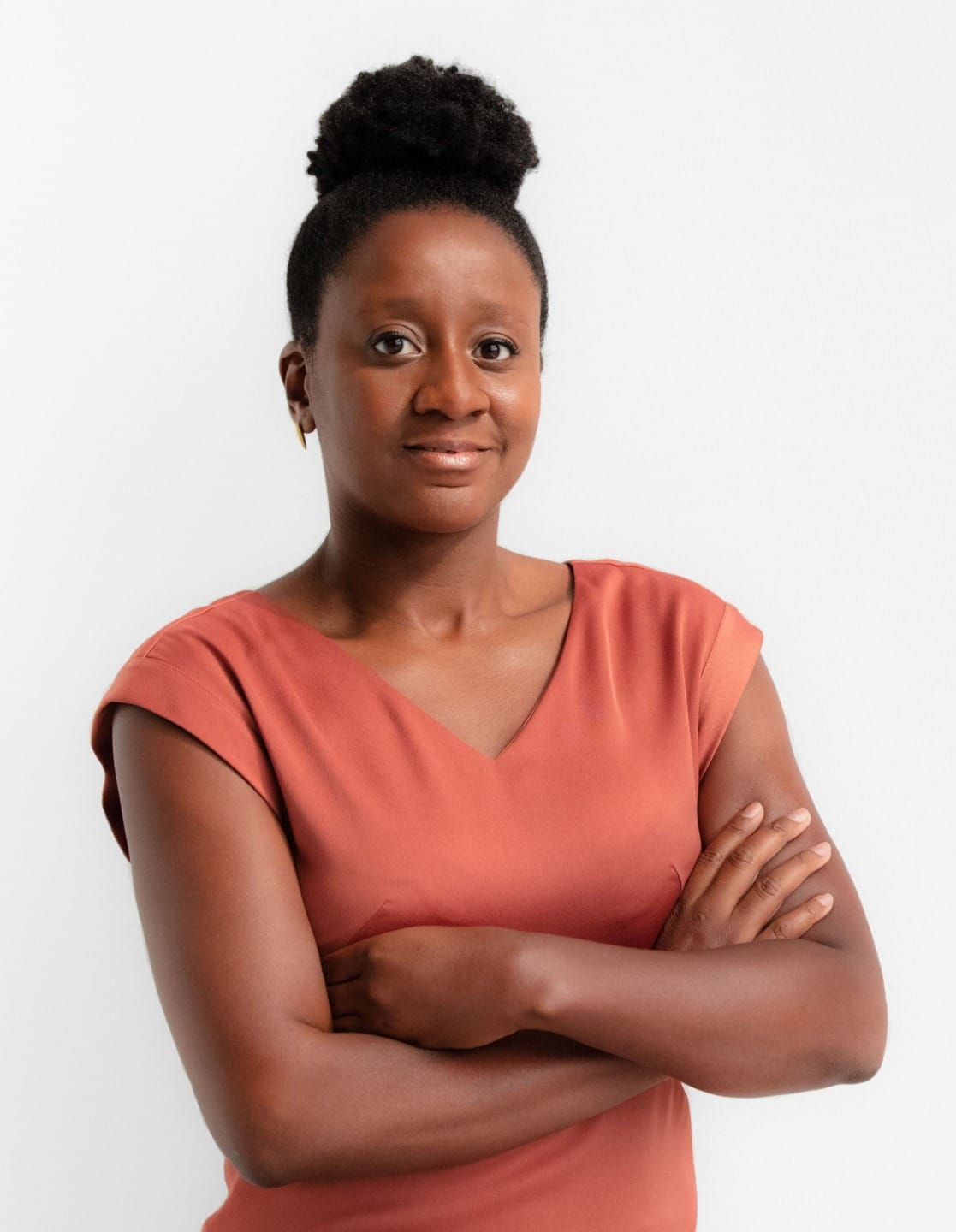 Person with arms crossed, wearing a rust-colored top, stands against a plain white background.