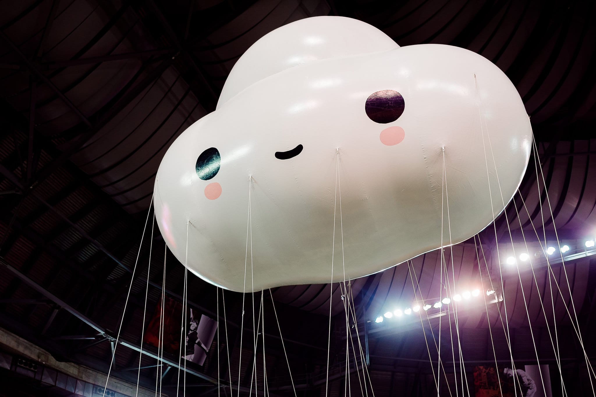 Cute cloud-shaped balloon with a smiling face floating indoors under ceiling lights.