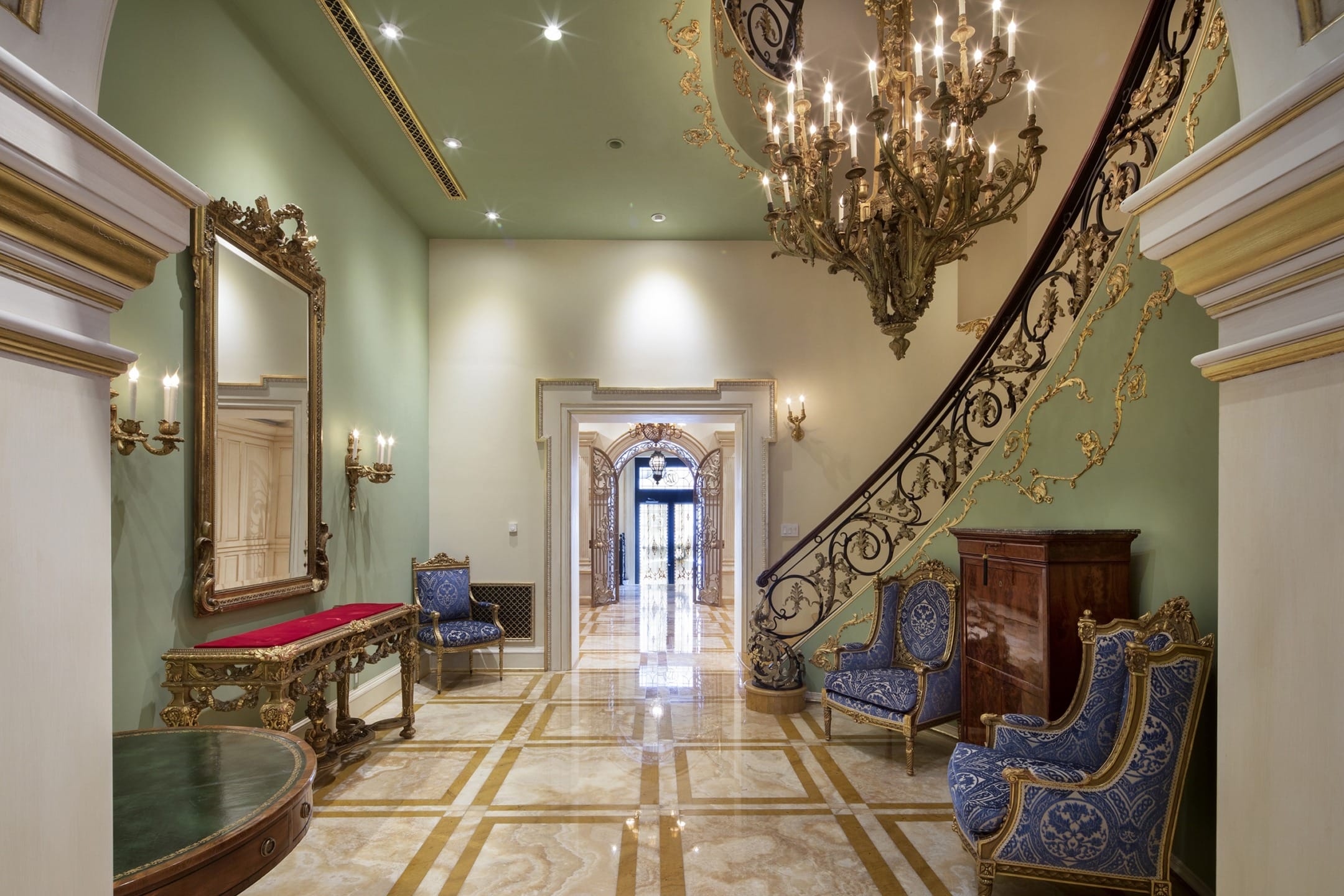 Elegant foyer with marble floor, ornate staircase, chandelier, and luxurious seating, exuding classic sophistication.