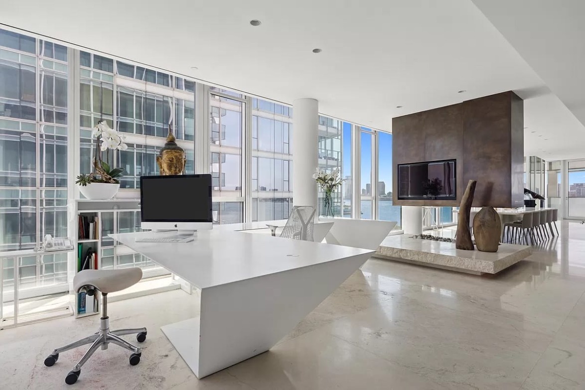 Modern minimalist office with a white desk, computer, chair, and large windows overlooking a cityscape.