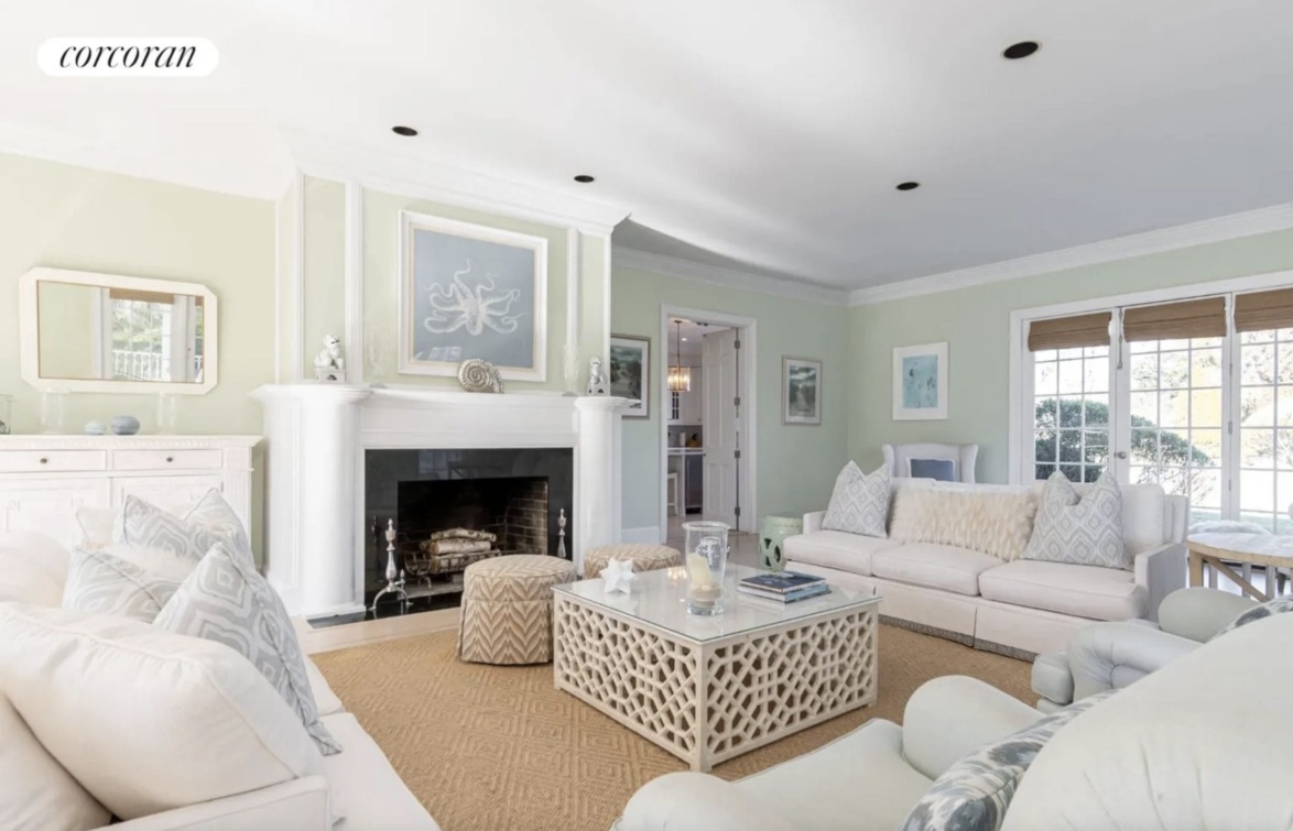 Elegant living room with white sofas, a fireplace, and large windows letting in natural light. Cozy and stylish decor.