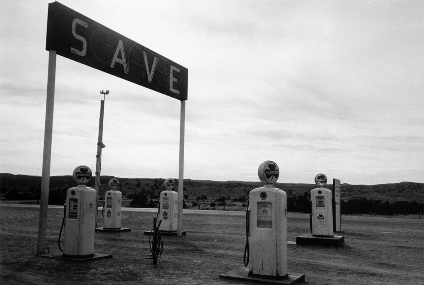 Vintage gas station with retro pumps under a SAVE sign, set against a barren landscape in black and white.