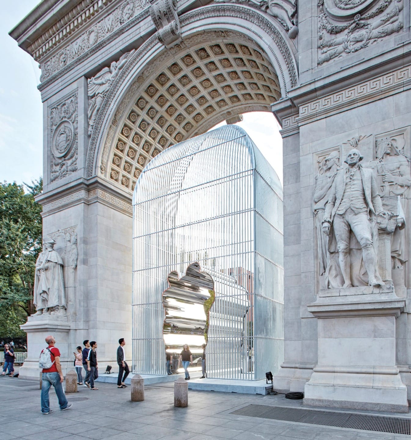 People walking near a modern art installation under a large stone arch in a city park setting.