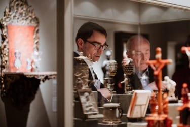 Two people examining decorative objects in a museum display case, showcasing ornate artifacts and intricate designs.