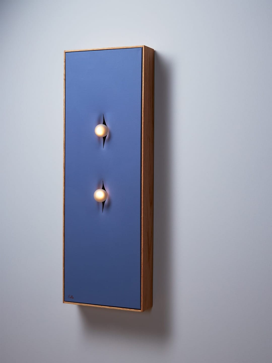 Modern wall art with two embedded light bulbs on a blue rectangular panel, framed in wood, mounted on a white wall.