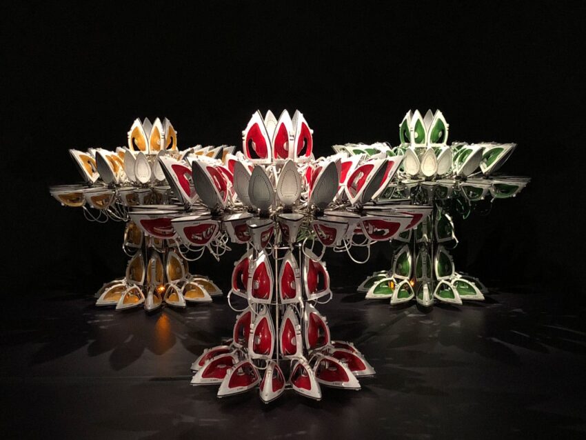 Colorful, lotus-shaped sculptures made from repurposed materials, illuminated in dark setting, showcasing sustainable art.