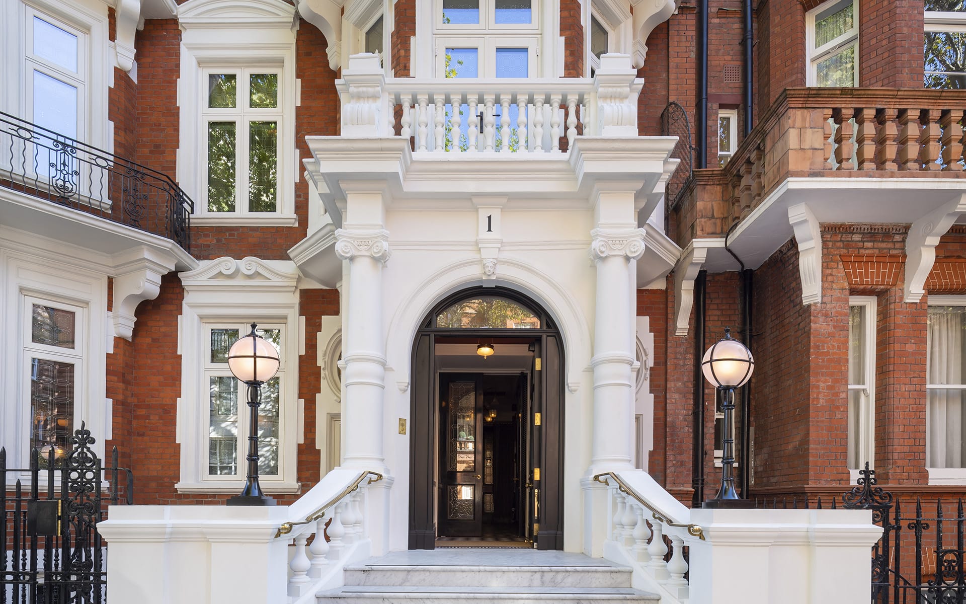 Entrance of an elegant red brick building with ornate white columns and two spherical lamp posts.