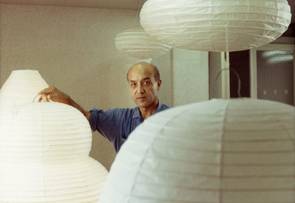 Person standing among large white paper lanterns in a softly lit room.