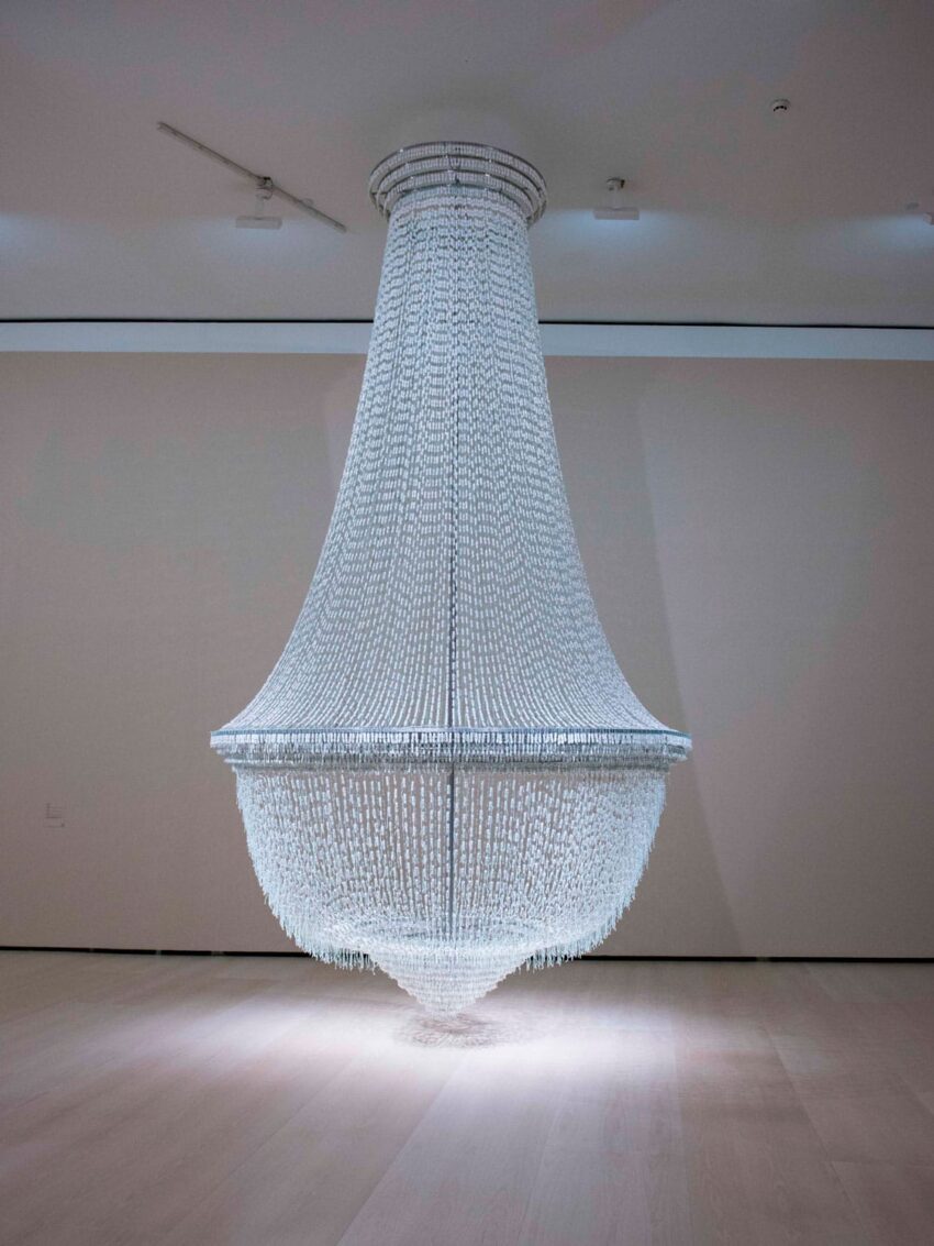 Large, elegant crystal chandelier displayed in a minimalistic room with a spotlight highlighting its intricate details.