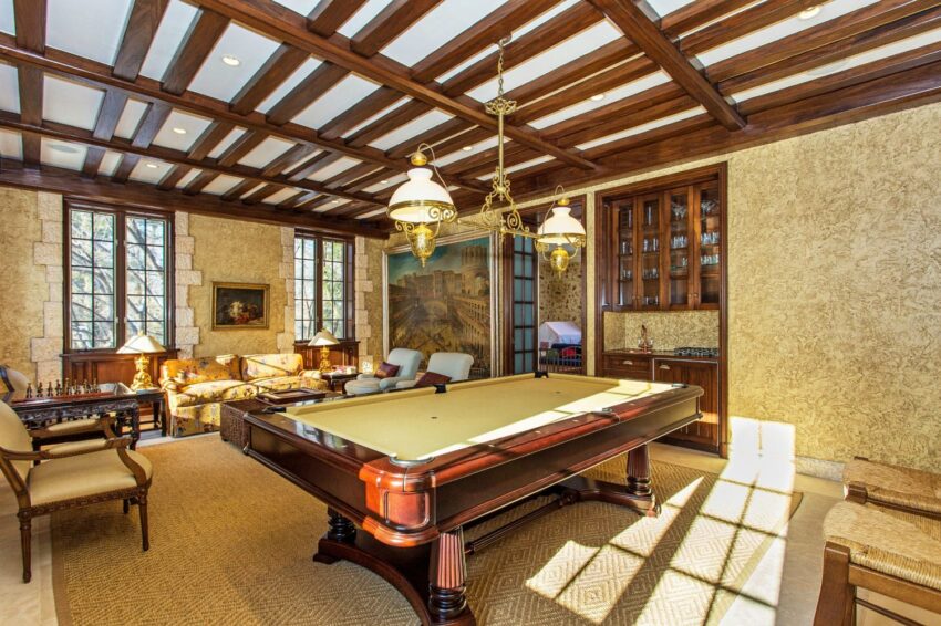 Luxurious game room with a billiards table, elegant wooden ceiling, large windows, and classic decor elements.