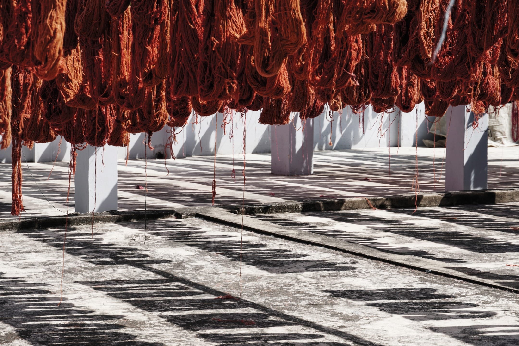 Drying red yarn hanging over a sunlit patterned surface in an outdoor area, creating an artistic contrast.