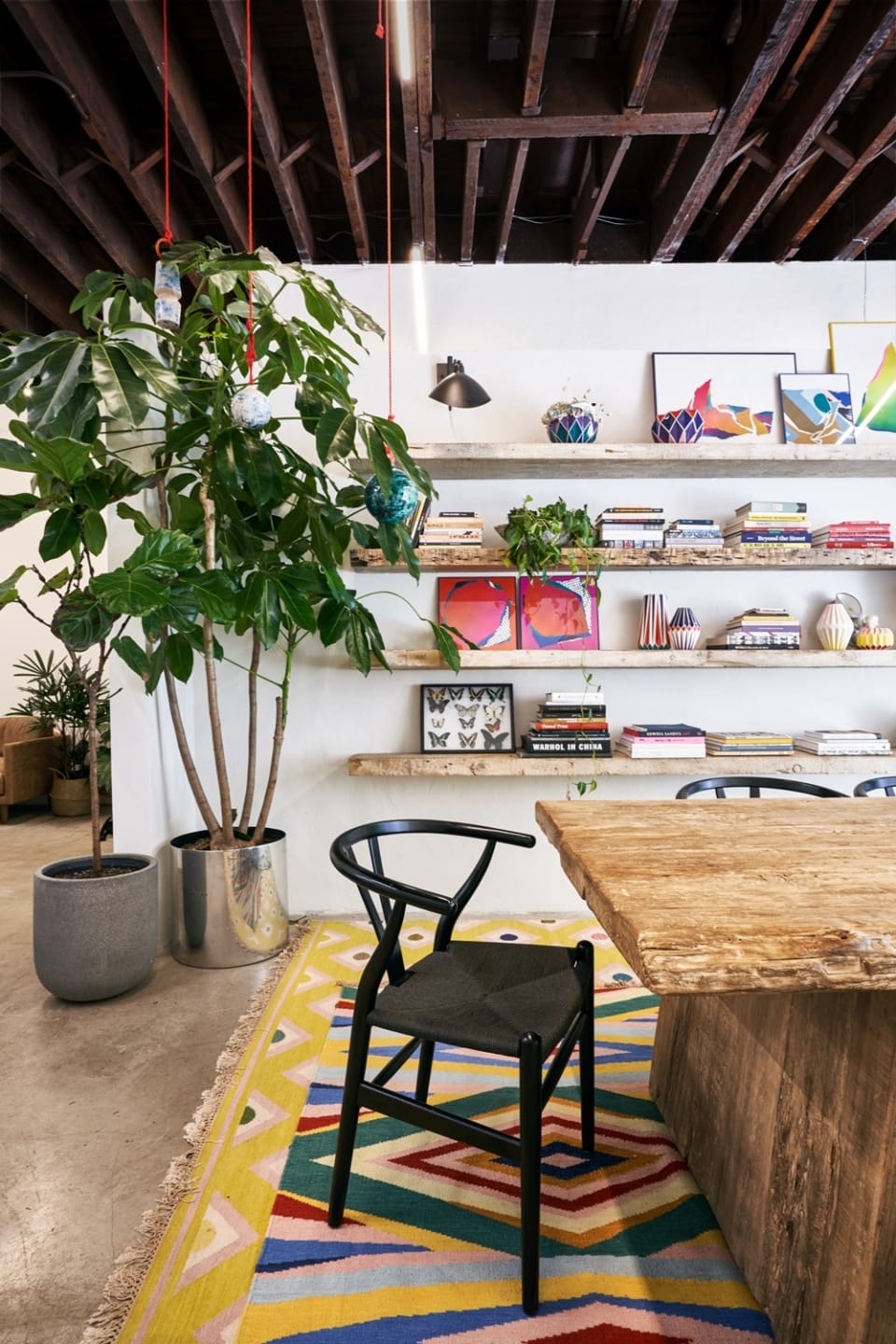 Modern office with a wooden desk, colorful rug, plant, and wall shelves displaying books and vibrant artwork.