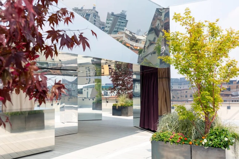 Rooftop with mirrored walls, colorful potted plants, and urban skyline in the background on a bright, clear day.