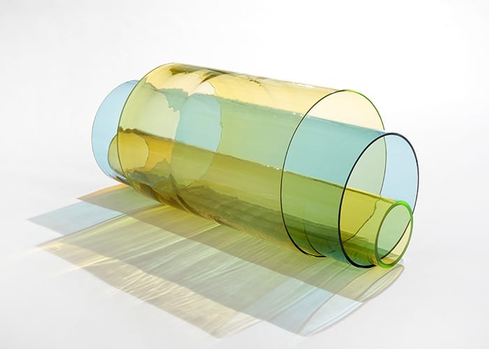 Colorful translucent glass cylinders intertwined, casting soft shadows on a white surface.