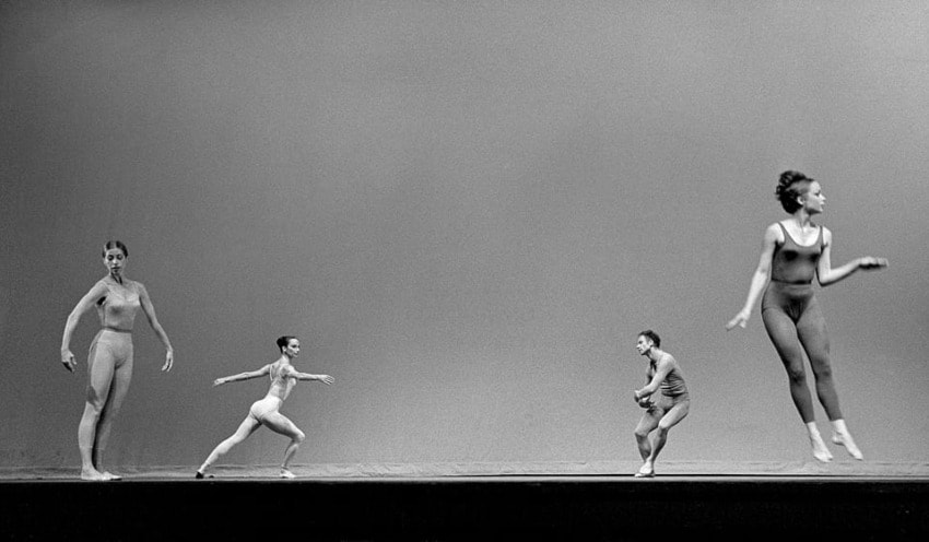 Dancers in motion performing a contemporary ballet on stage with a minimalist backdrop.
