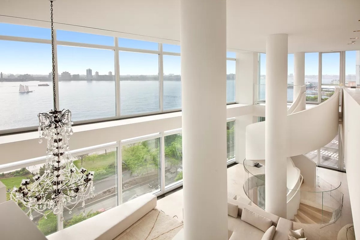 Luxurious penthouse interior with floor-to-ceiling windows, spiral staircase, and a view of the river and city skyline.