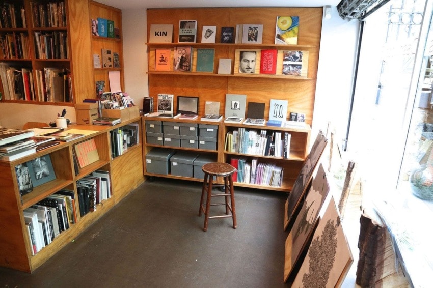 Cozy bookstore interior with wooden shelves filled with books, art displayed, and a stool in the middle of the room.