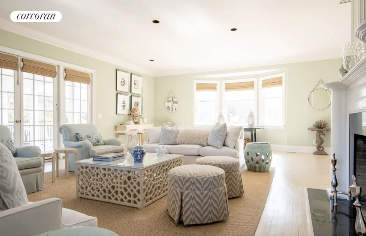 Spacious, sunlit living room with pastel decor, large windows, and modern furniture.