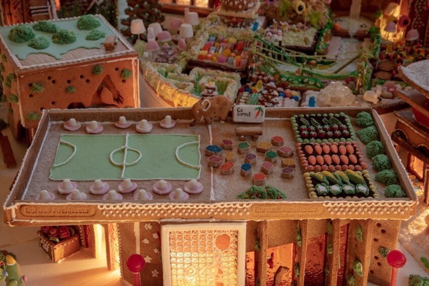 Gingerbread house with a candy soccer field, colorful garden, and an elephant cookie on the roof.